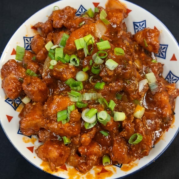 Spicy chili chicken, garnished with fresh green onions, served in a decorative white bowl.