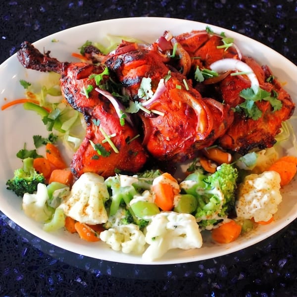 Tandoori chicken drumsticks with cilantro, onions, and a side of mixed vegetables with dressing.