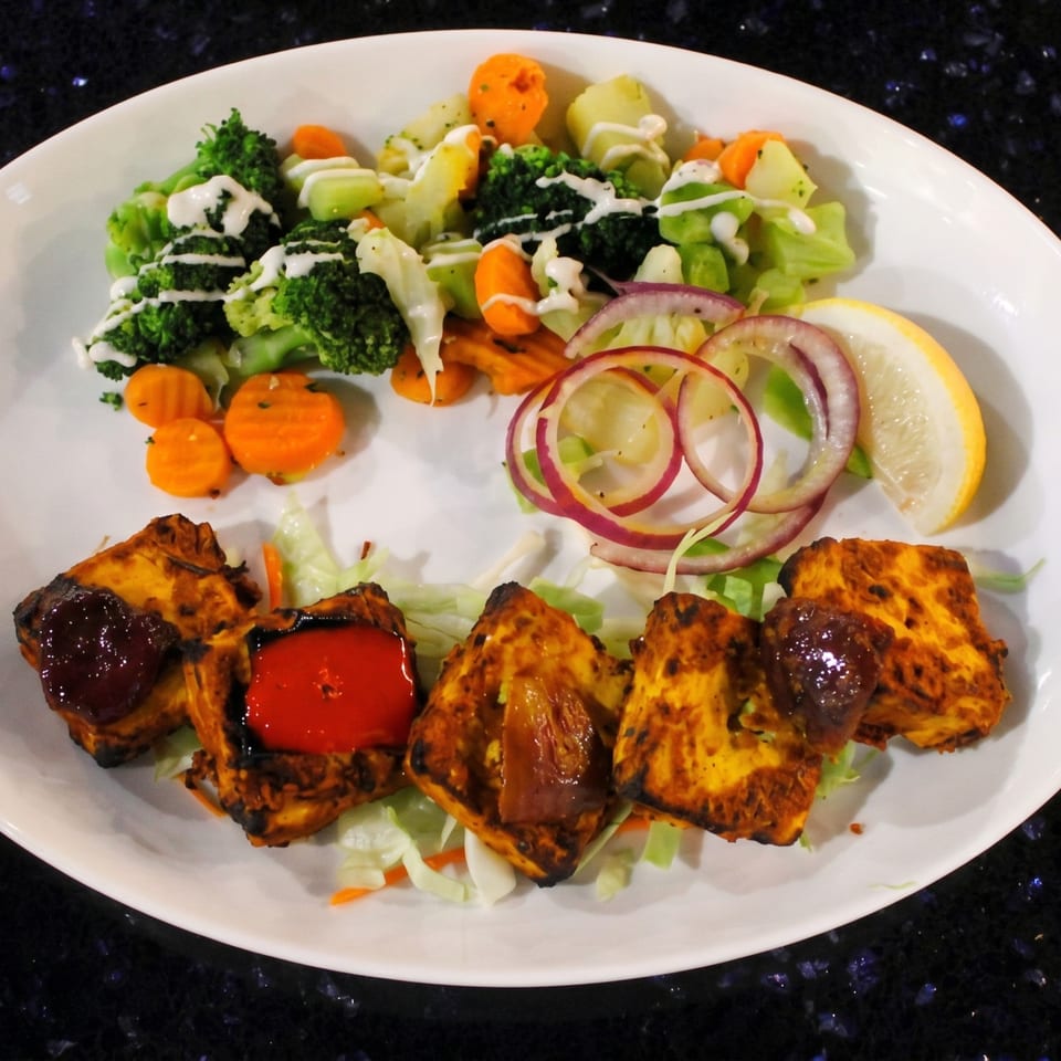 Grilled paneer with sauces, a side of broccoli, carrots, onions, and a lemon wedge.