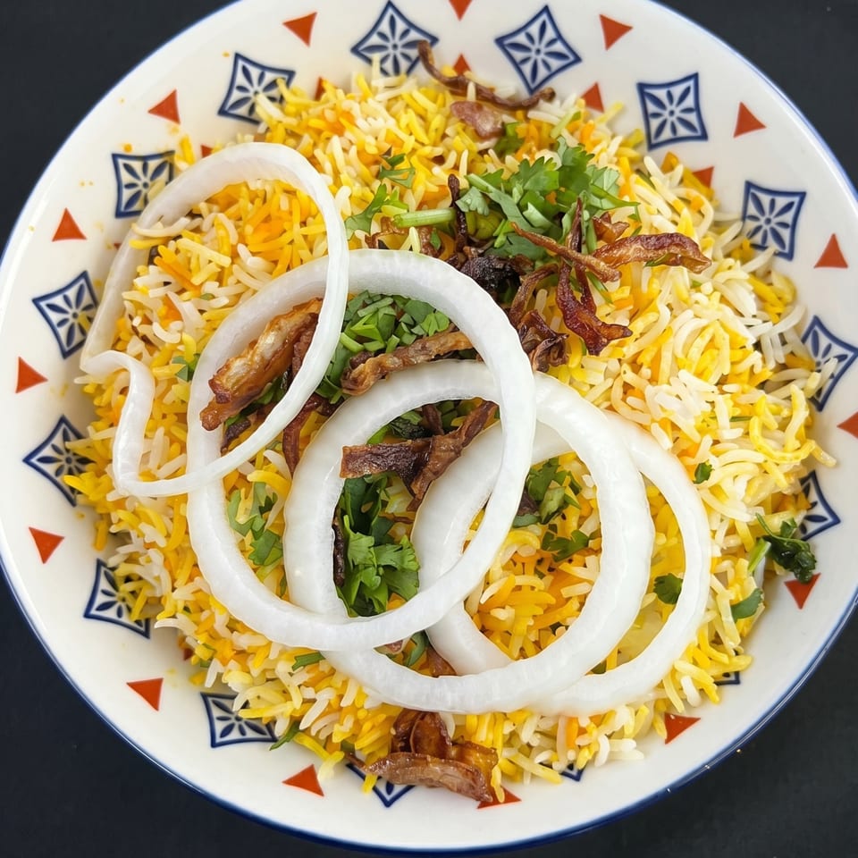 A colorful bowl of biryani rice, garnished with fresh cilantro, fried onions, and raw onion rings.
