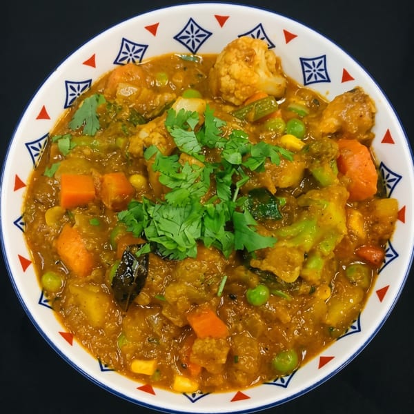 A colorful vegetable curry with cauliflower, carrots, peas, and cilantro in a decorative bowl.