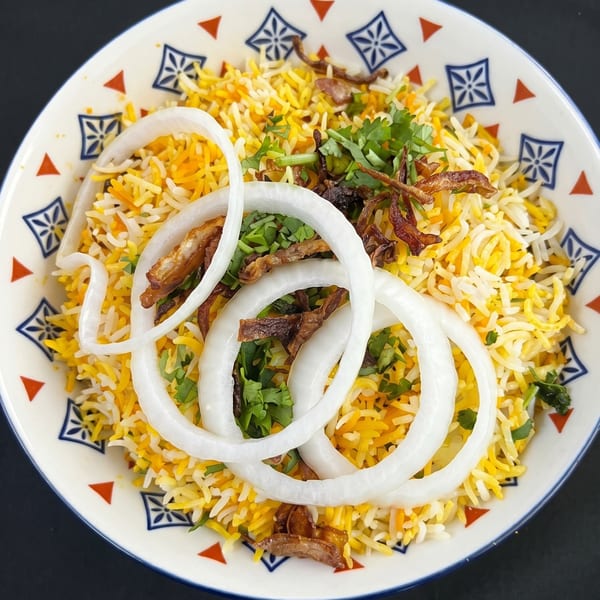 Close-up of biryani rice with fried onions, fresh cilantro, and raw onion rings in a decorative bowl.